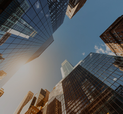 Upward view of tall skyscrapers with glass facades reflecting the sky and nearby buildings.