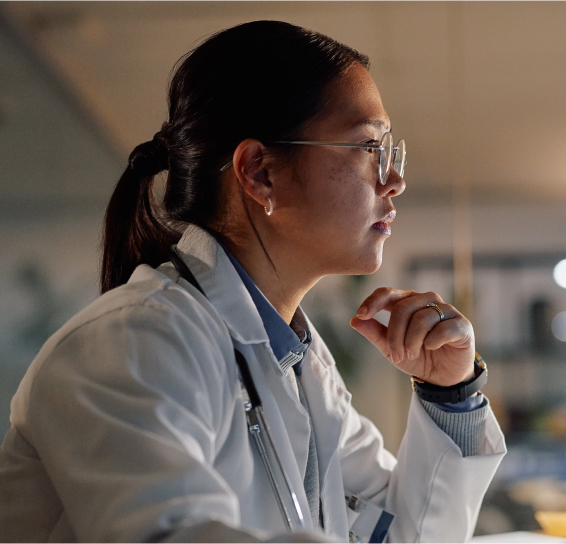 Person in a lab coat and glasses, seated in profile view with a thoughtful expression.