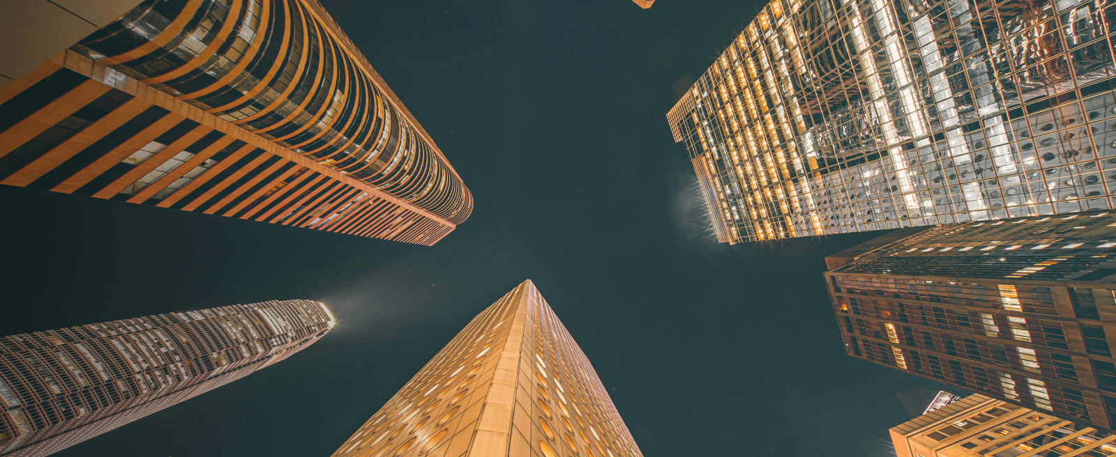 Upward view of illuminated skyscrapers in Asia at night against a dark sky.