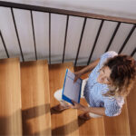 Person walking up a wooden staircase, holding a blue folder.