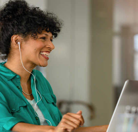 Person wearing earphones, smiling at a laptop in an office setting.