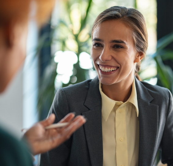 Smiling woman in a grey blazer in a bright setting, engaging in conversation.