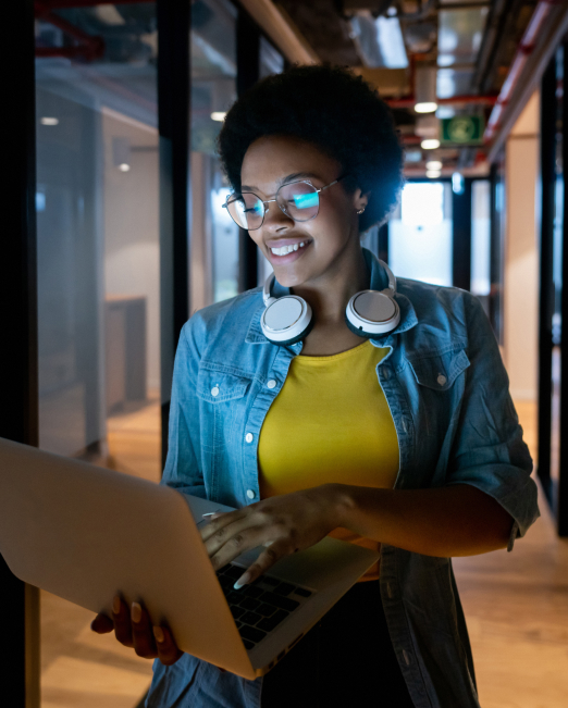 Person smiling while using a laptop in a hallway with glass walls.