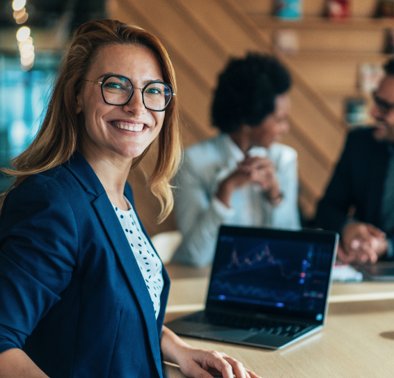 Woman in blue blazer smiling in an office with a laptop showing a graph.