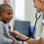 Healthcare professional using a stethoscope on a smiling child.