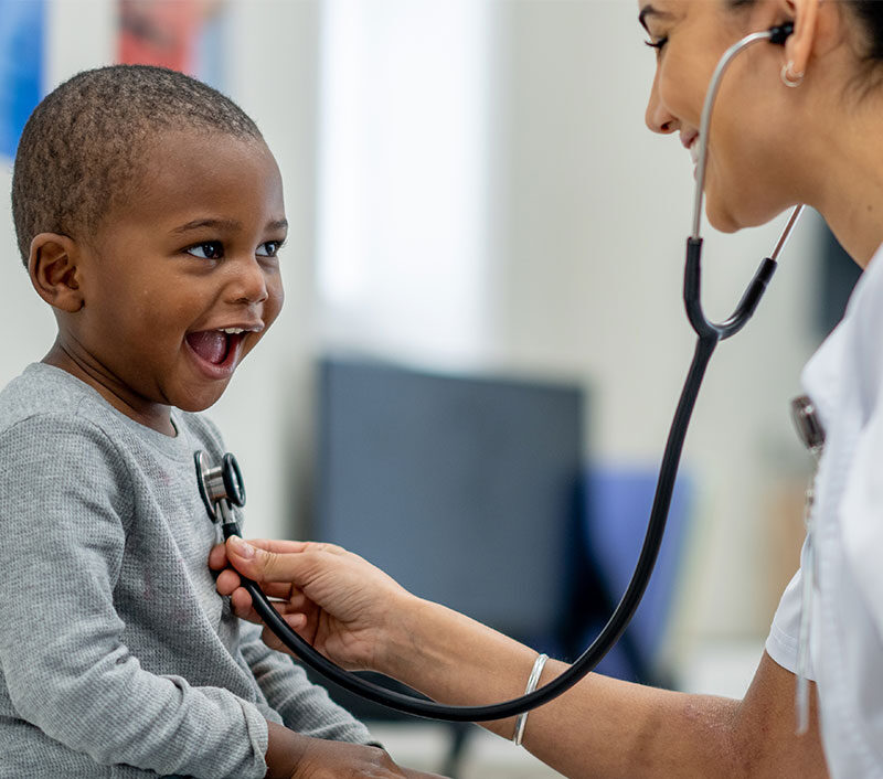 Healthcare professional using a stethoscope on a smiling child.