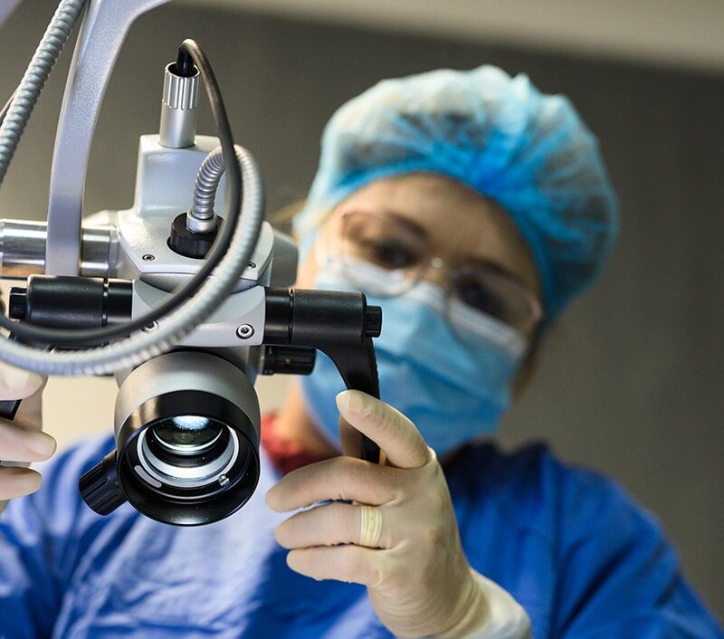 A healthcare worker adjusts a surgical microscope in a medical setting.