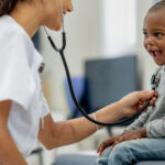 Healthcare professional using a stethoscope on a smiling child.