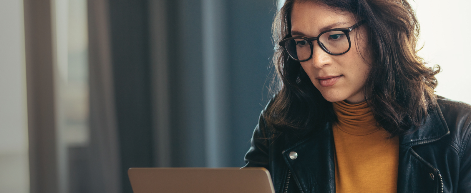 Person in glasses working on a laptop at a wooden table.