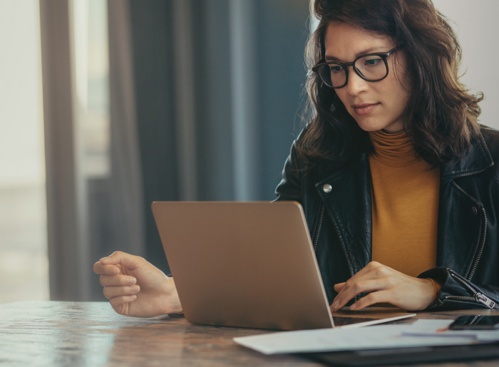 Person in glasses working on a laptop at a wooden table.