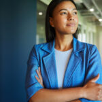 Woman in a blue blazer standing with arms crossed, indoors.