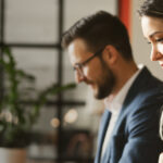 Two people working at a table in a modern office space, focusing on their tasks.