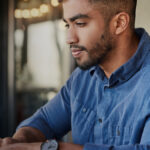 Man in a blue shirt working on a laptop indoors.