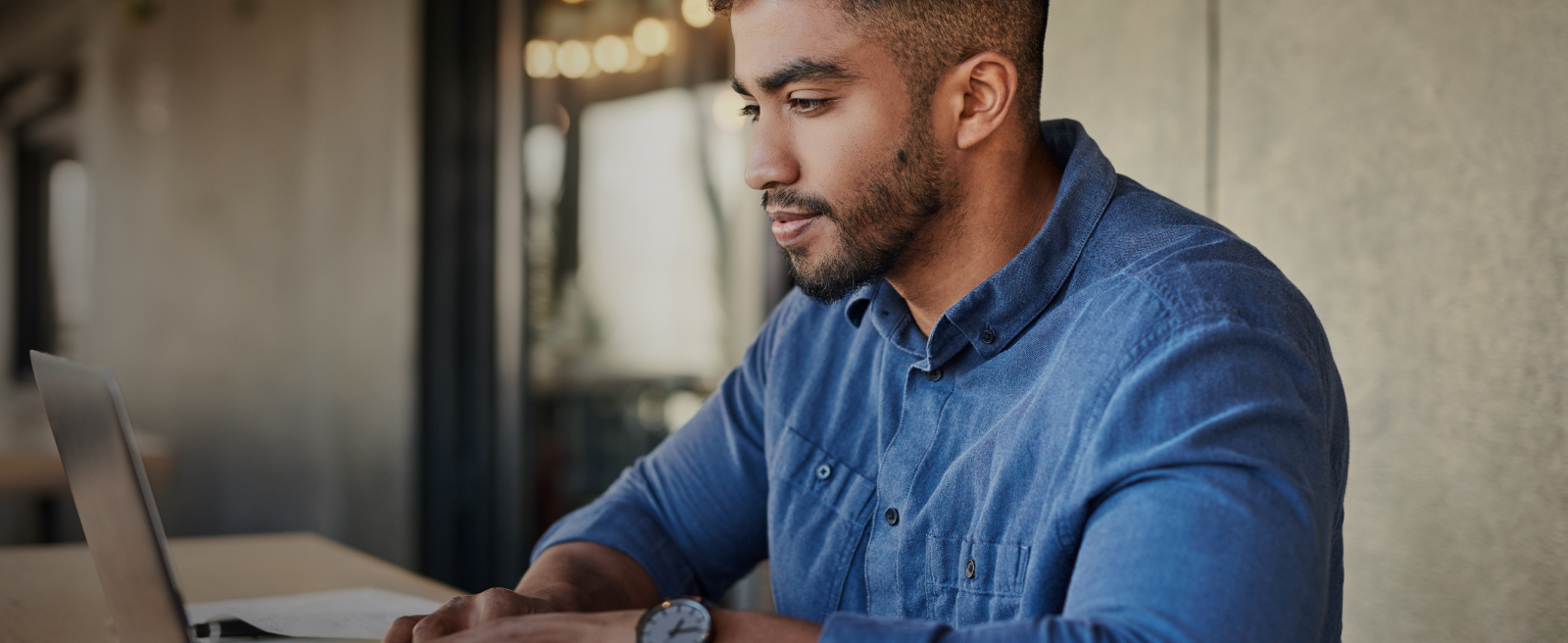 Man in a blue shirt working on a laptop indoors.