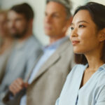 Attentive woman seated with others in a professional setting.