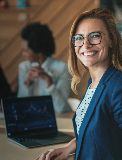 Woman in blue blazer smiling in an office with a laptop showing a graph.