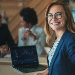 Smiling woman in a blue blazer with a laptop in front of her.