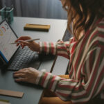 Person working on a tablet with charts and graphs, using a stylus at a desk.