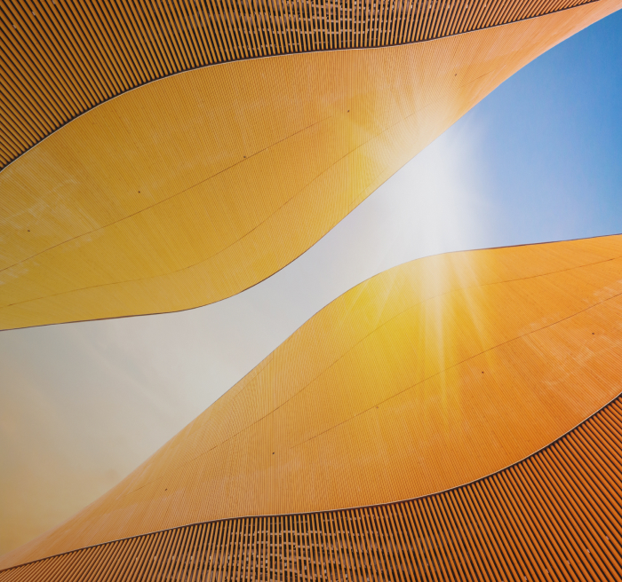 Curved golden-orange architectural panels against a blue sky with sunlight streaming through.