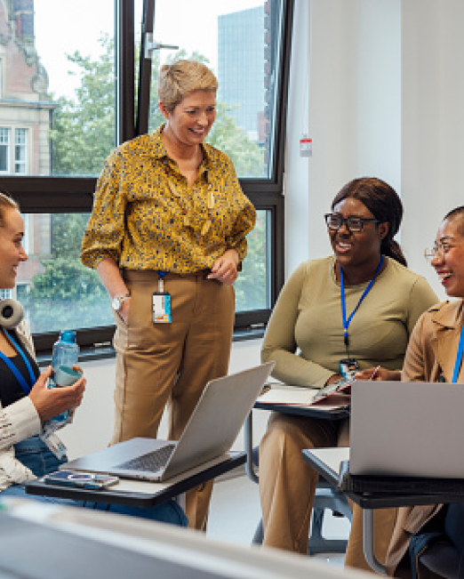 Group of four people in a meeting with laptops, smiling and interacting.