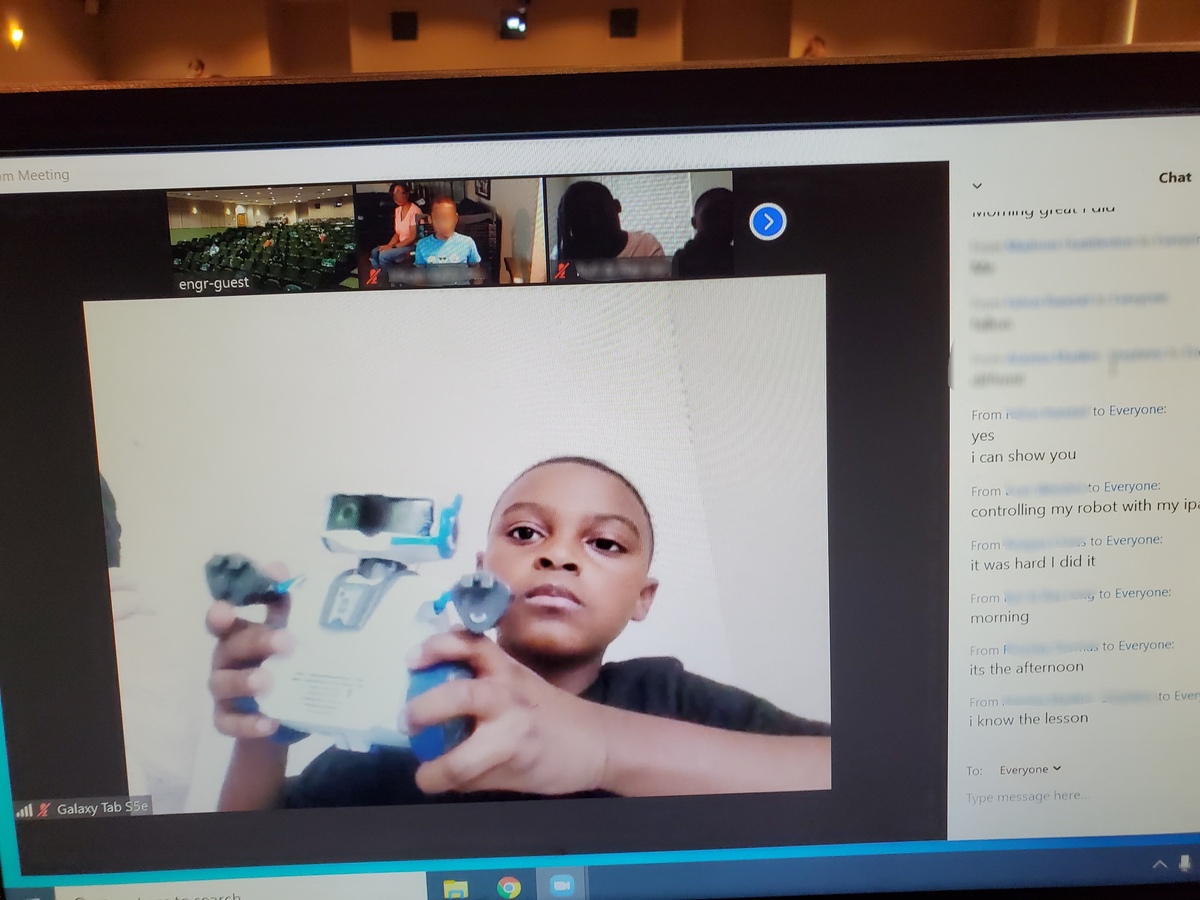 A child demonstrates a robot during a video conference, with chat messages visible on the side.