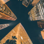 Upward view of illuminated skyscrapers in Asia at night against a dark sky.