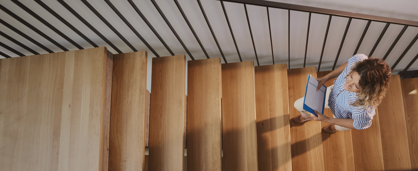 Person climbing a wooden staircase, seen from above, holding a blue notebook.