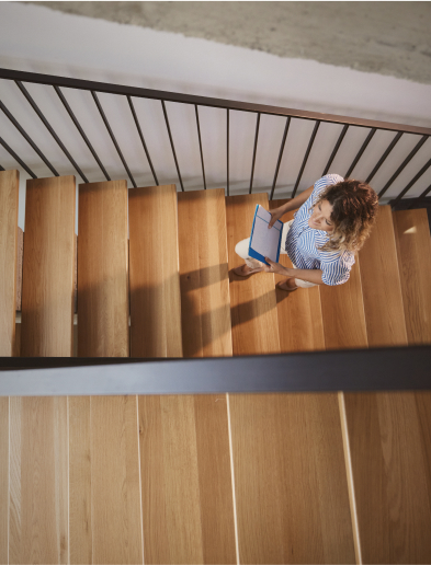 Person climbing a wooden staircase, seen from above, holding a blue notebook.