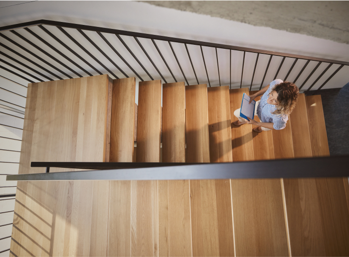 Person climbing a wooden staircase, seen from above, holding a blue notebook.