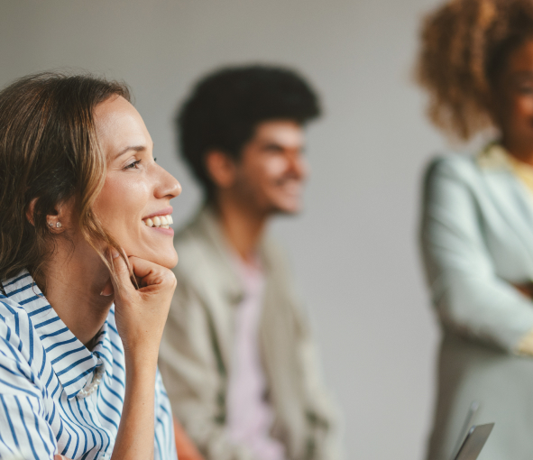 A woman smiles in profile with two other smiling people out of focus in the background behind her