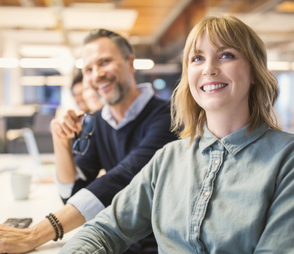 Coworkers at a conference table smile while watching a presentation