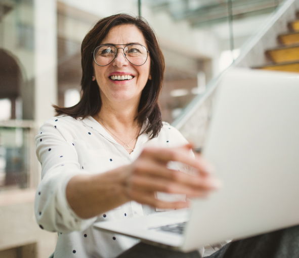 A woman smiles while looking off to the left and adjusting her laptop screen