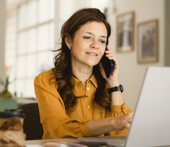 A woman talks on the phone while gesturing at her laptop screen