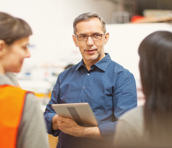 A manager holding a tablet talks to warehouse employees