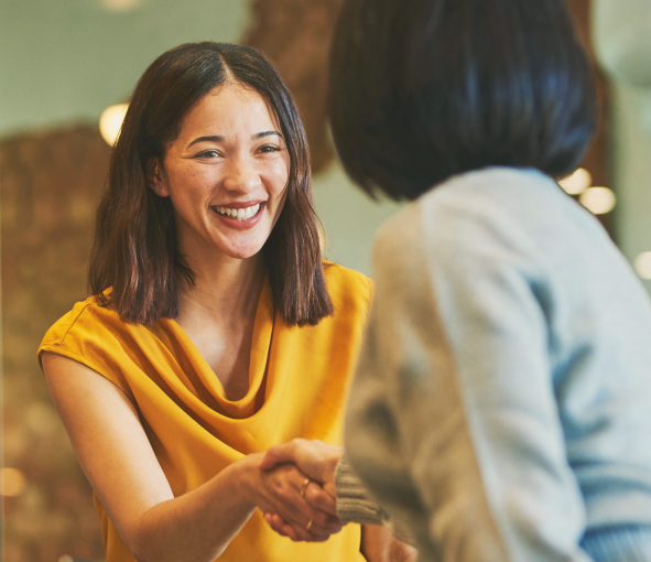 A woman smiles and shakes another woman's hand