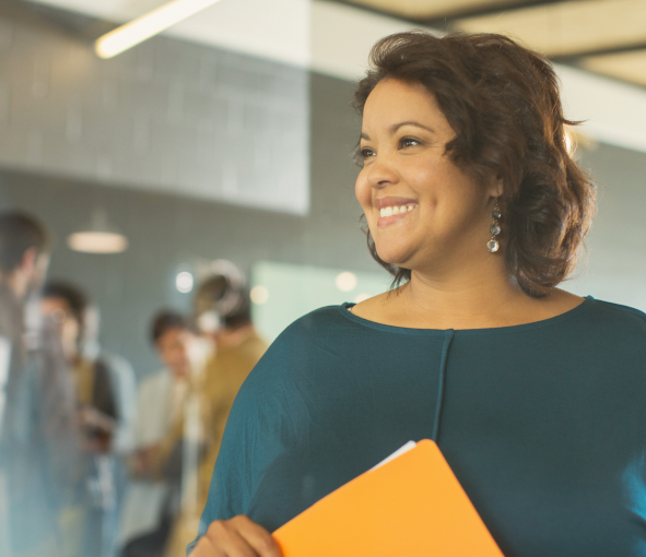 A woman holding a manila envelope in an office smiles