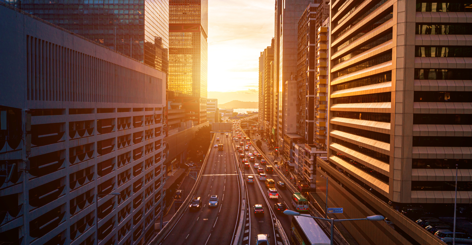 Sunset over a city street flanked by tall buildings with traffic on the road.