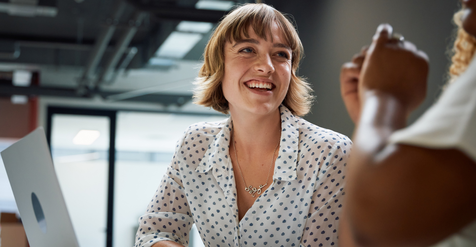 A young woman smiling at a coworker in a modern office setting.