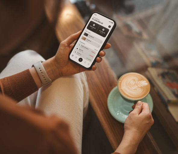 A closeup of a hand holding a phone with a banking app open and also holding a latte