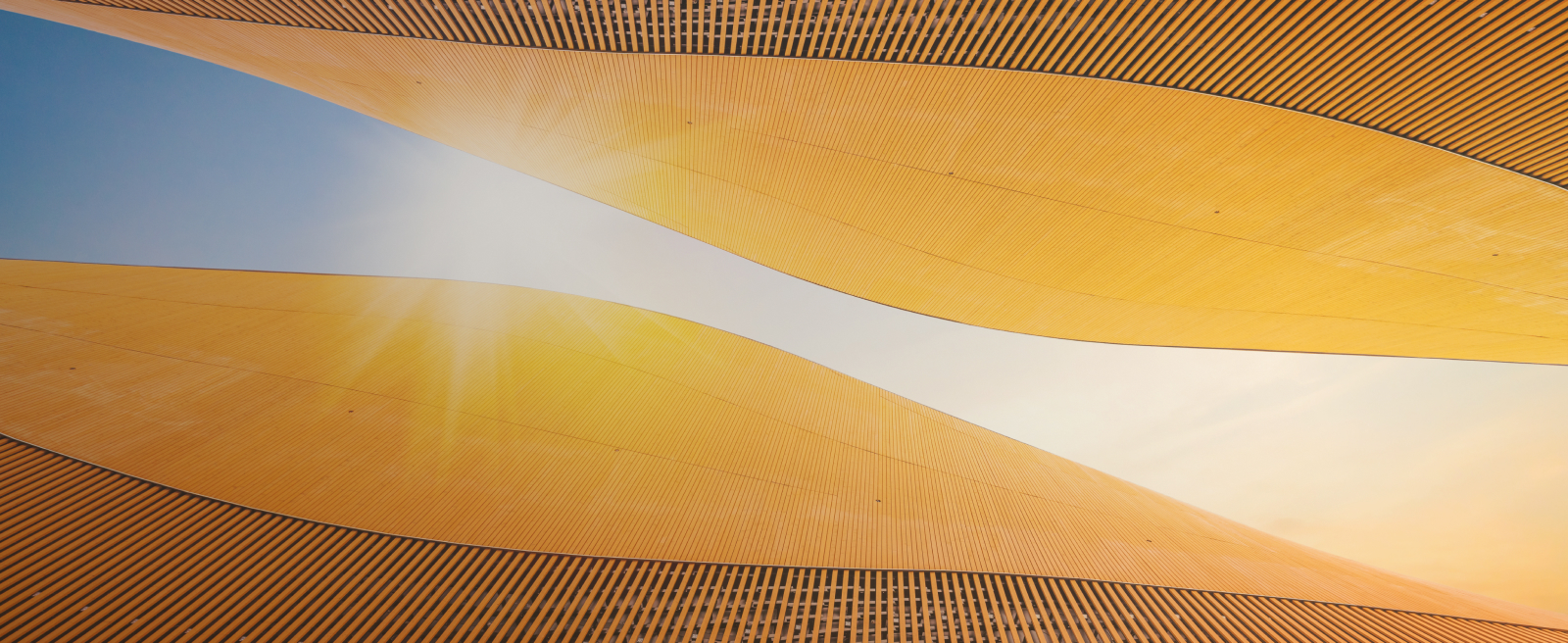 Curved golden-orange architectural panels against a blue sky with sunlight streaming through.