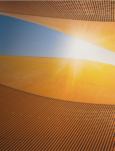 Curved golden-orange architectural panels against a blue sky with sunlight streaming through.