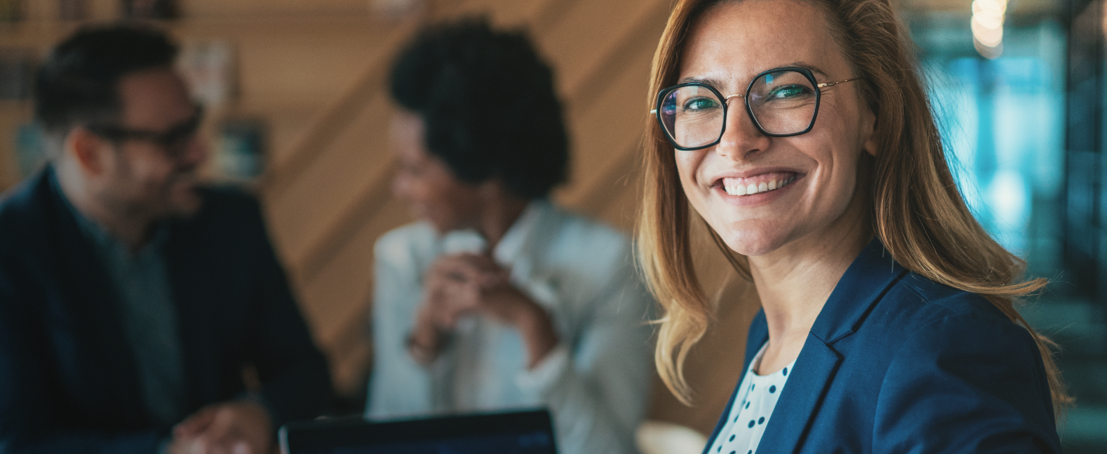 Woman in blue blazer smiling in an office with a laptop showing a graph.