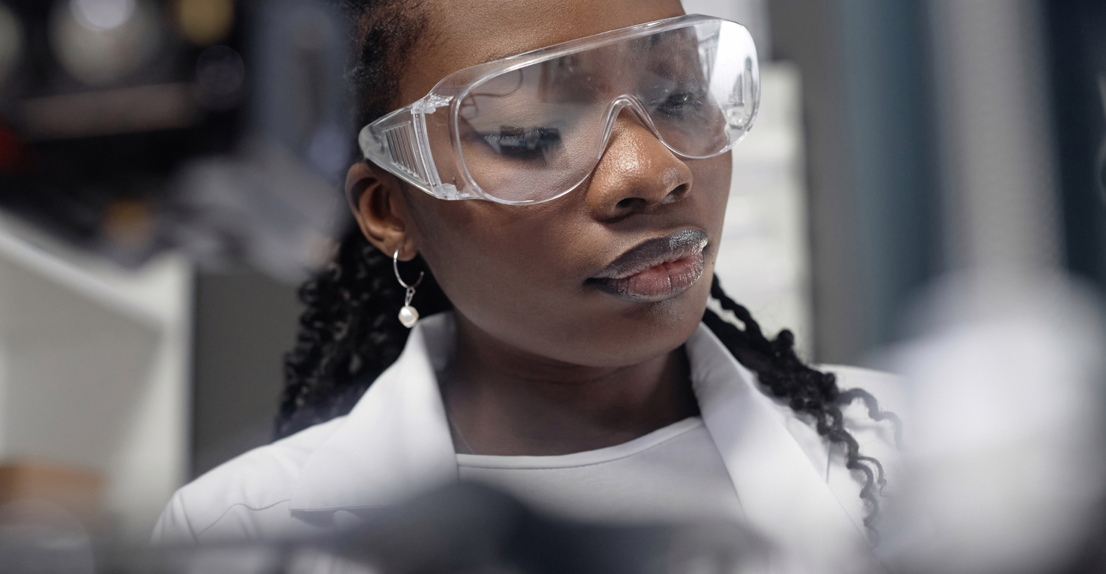 Person wearing protective goggles and a lab coat in a laboratory.