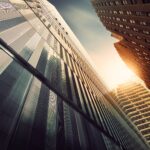 Upward view of three skyscrapers with the sun shining through a gap between them.