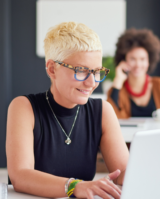 A woman in an office smiles as she works on a laptop