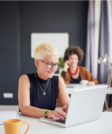 A woman in an office smiles as she works on a laptop