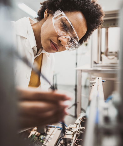 A woman in a lab wearing safety glasses performs an experiment