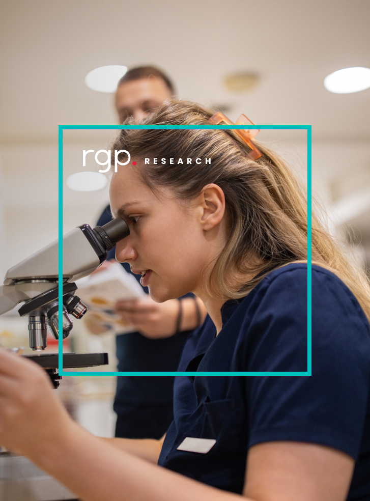 A woman wearing scrubs in a laboratory looks intently into a microscope