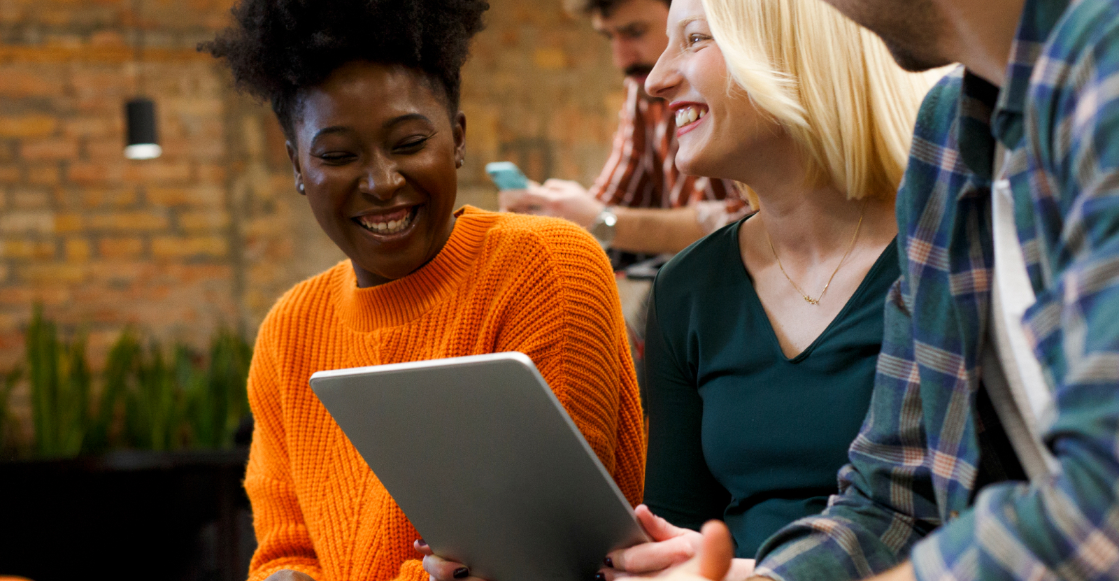 Three people sitting together, smiling and talking, one holding a tablet.