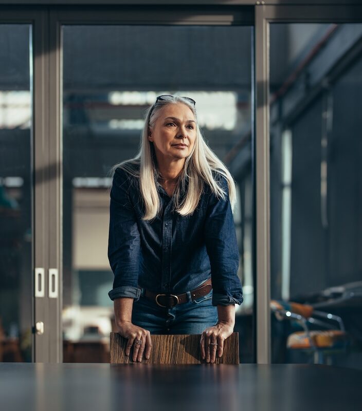 Woman leaning on a chair next to a table, looking off into the distance